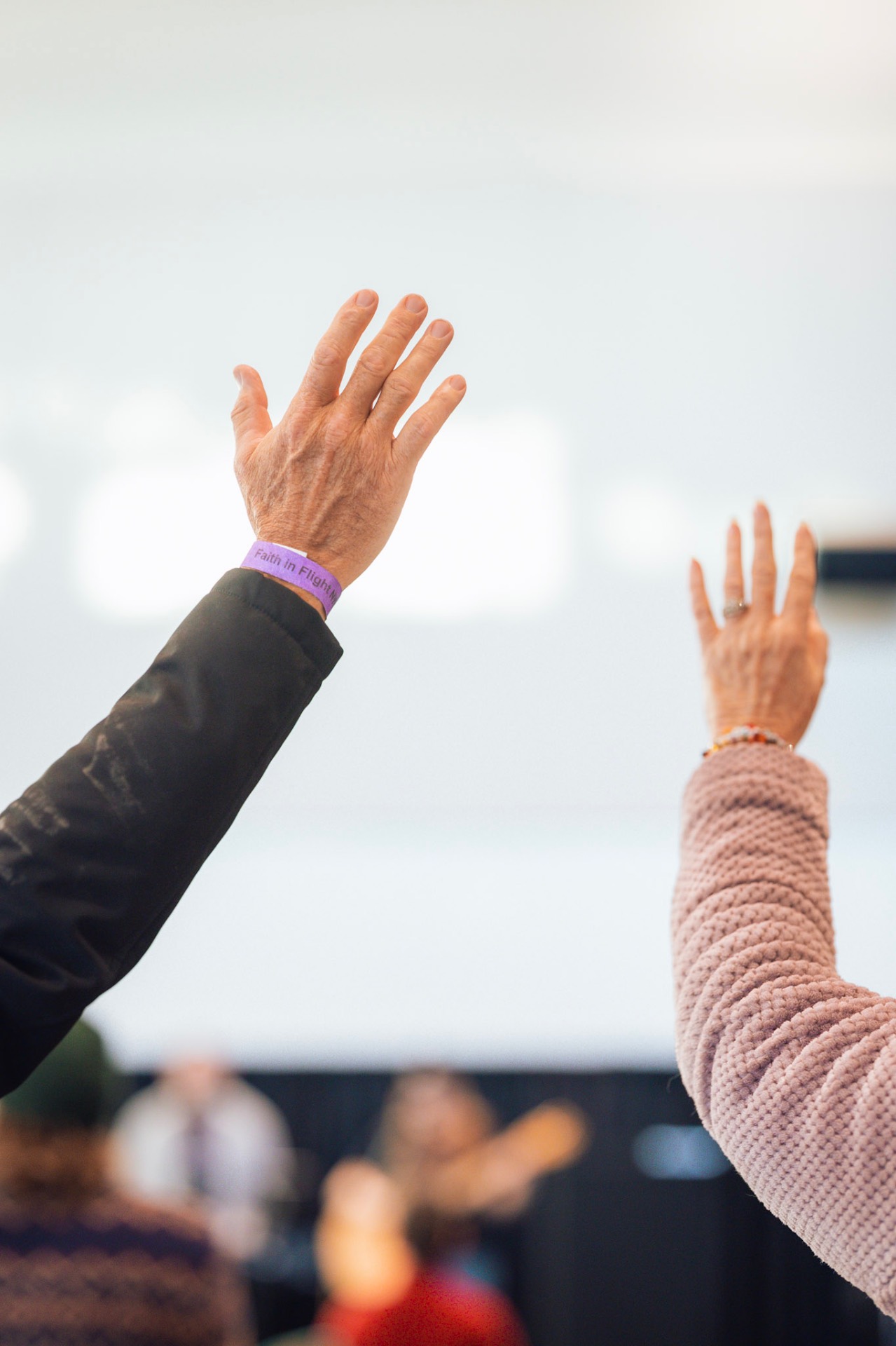 Hands raised wearing Faith In Flight wristband